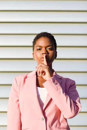Female in pink suit making “shhh” gesture