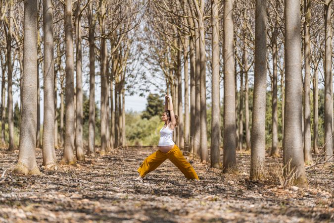 Adult expectant mother practicing yoga in park during sunny day