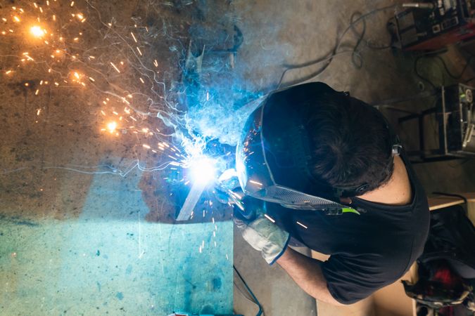 Welder in protective helmet welding metal detail in workshop