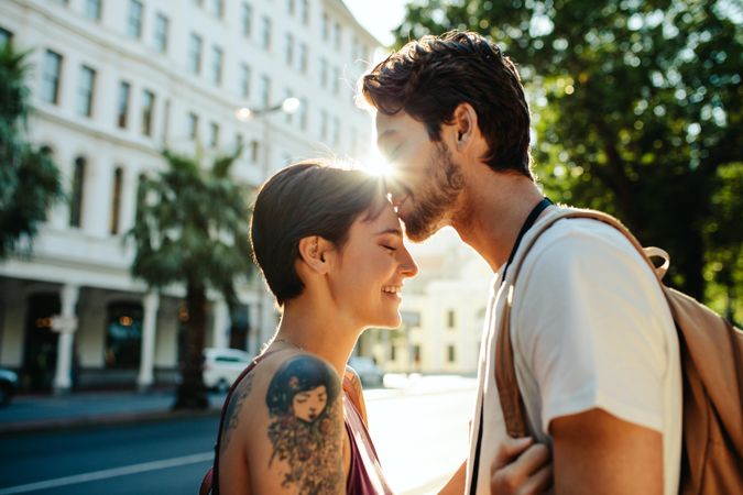 Man kissing woman on forehead standing on the street with sun in the background