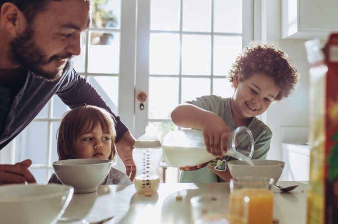 Man watching his child pour milk in his breakfast bowl
