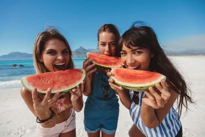 Group of females taking bites of watermelon slices on the beach