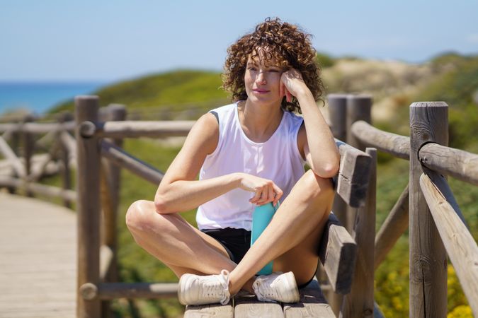 Smiling woman sitting on fence with water bottle