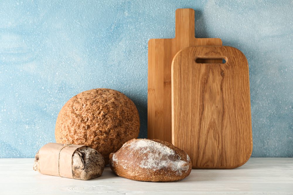 Bakery products and cutting boards on wooden table against light background, space for text