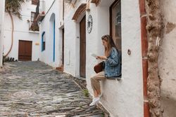 Full length of woman sitting on window ledge with a paper map in village