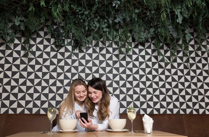 Women friends using smartphone at restaurant table