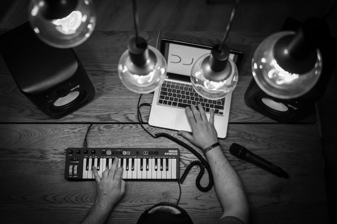 Grayscale photo of person creating music using digital keyboard and laptop indoor