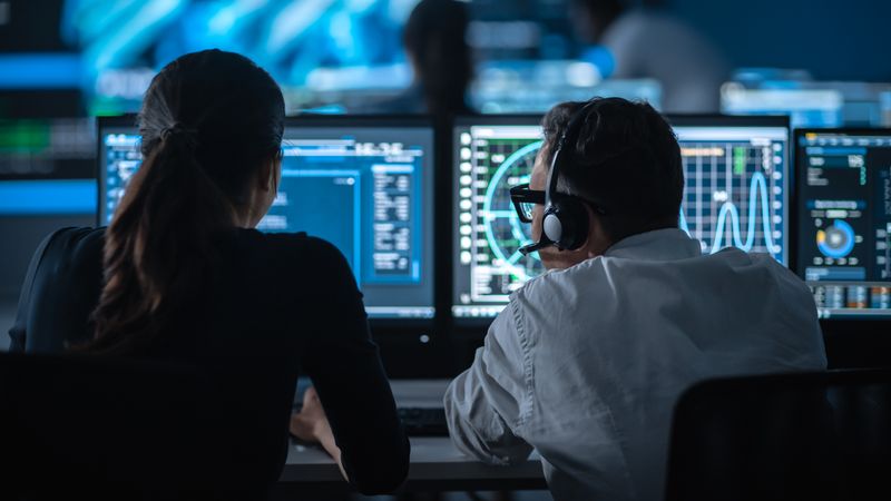 Cybersecurity Experts Monitor Data on Multiple Screens in Dimly Lit Control Room.