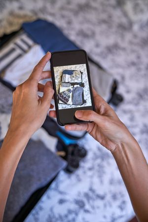 Crop traveler taking photo of opened suitcase