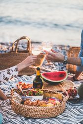 Two hands toasting with wine glasses over summer picnic by the ocean