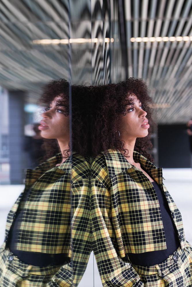 Stylish Black woman reflecting on glass wall in town
