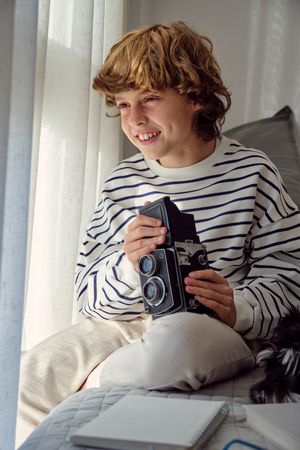 Cheerful boy with retro photo camera on bed