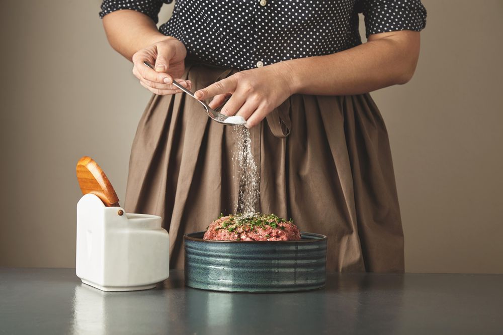 Woman sprinkling spoon of salt onto ground meat
