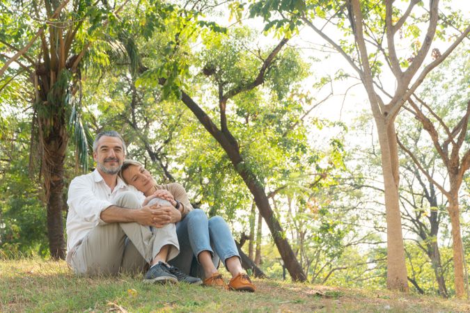 Happy mature woman leaning her head on man’s shoulder while sitting in park