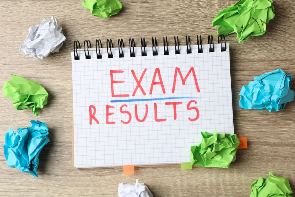 Top view of open notebook with the word “exam results” with glasses and stationary