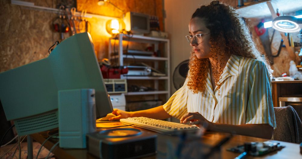 Hispanic Female Engineer Using Old Desktop Computer In Nineties Retro Garage In The Evening.