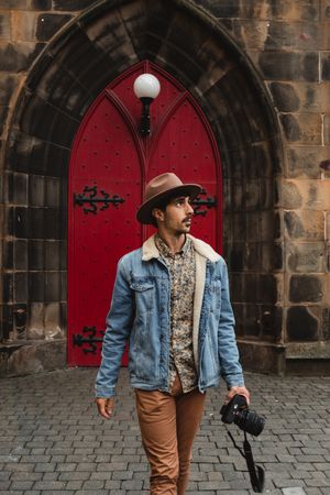 Adult pensive tourist with camera against arched doorway of medieval fortress