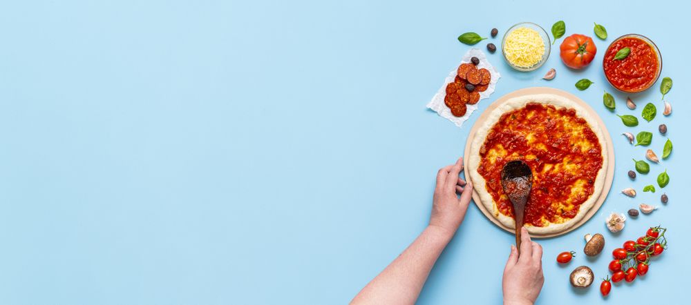 Putting tomato sauce on raw pizza dough