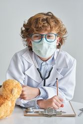 Boy doctor in sterile mask with stethoscope and toy bear