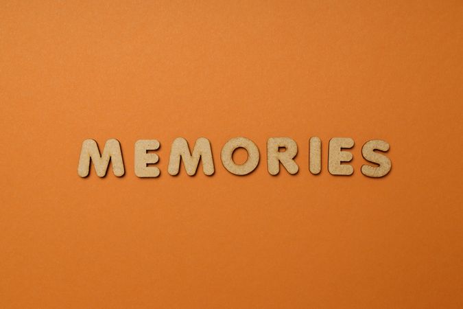 The word “Memories” written in cork in center of dusty orange background, copy space