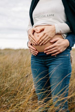 Pregnant couple making heart with hands on belly