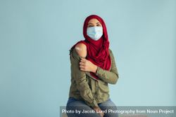 Muslim female after receiving corona virus vaccination sitting against blue background 0Jkop5