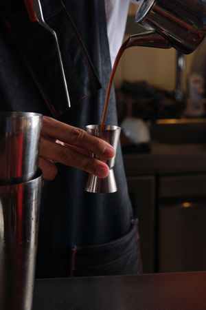 Crop bartender pouring coffee from kettle into jigger