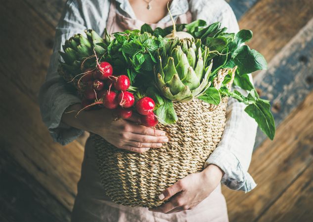 Female gardener holding basket of garden herbs and vegetables