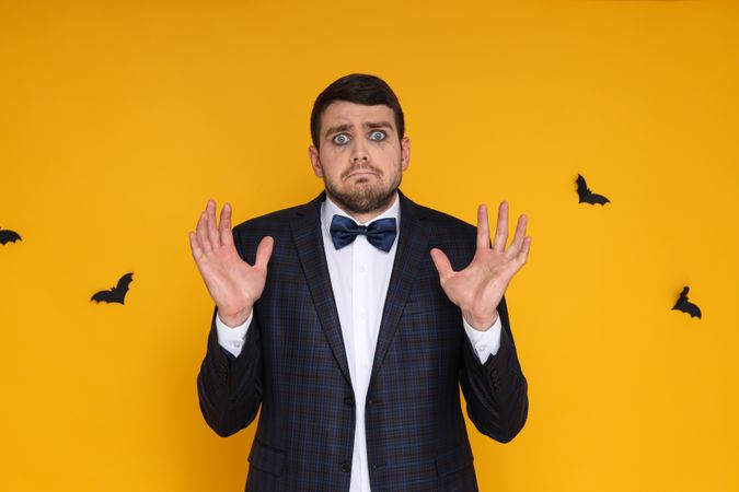 A man in a business suit with zombie makeup on a yellow background, scared