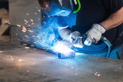 Welder in protective helmet welding metal detail in workshop