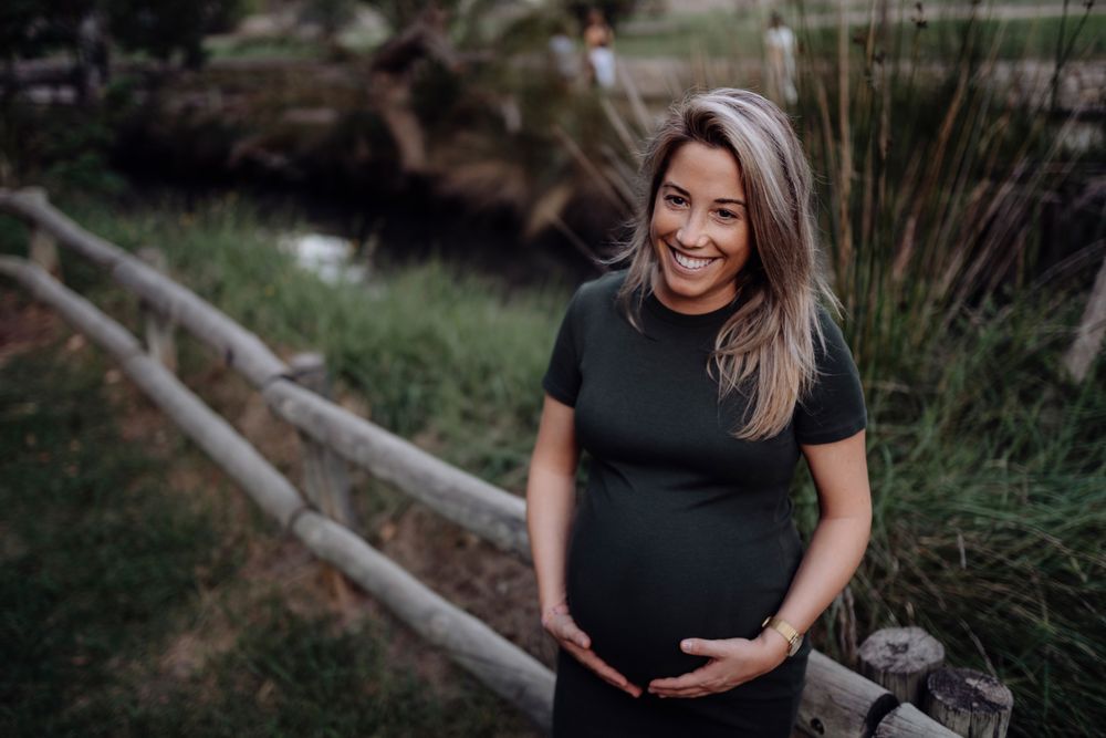 Happy pregnant woman standing at river in park