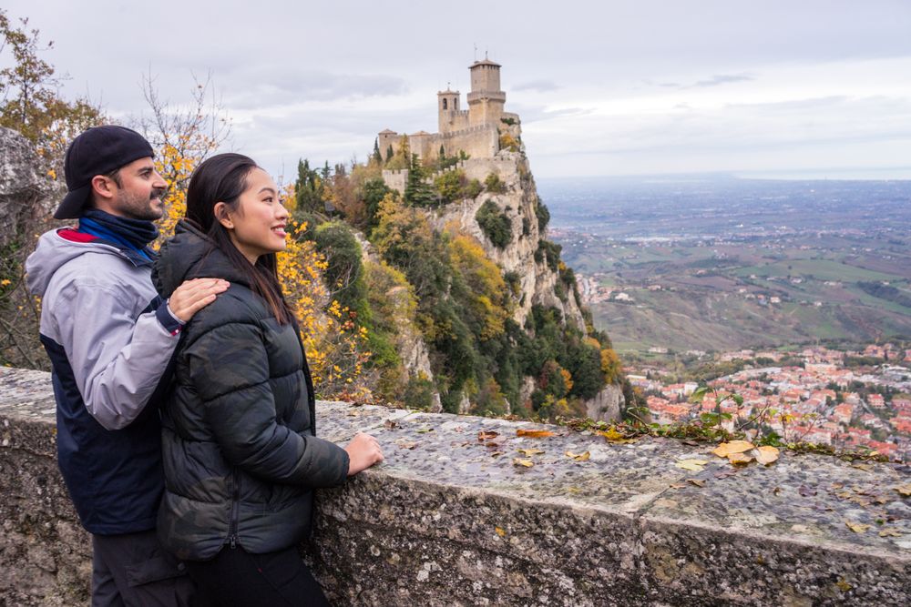 Lovely cheerful multiracial couple bonding near by stony fence viewing on castle on hill