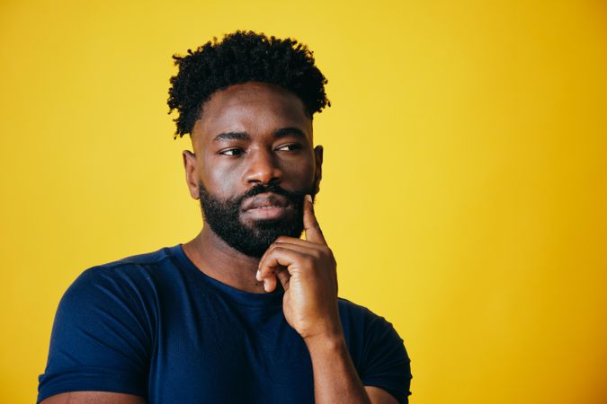 Portrait of thoughtful Black man with hand to his temple on yellow background