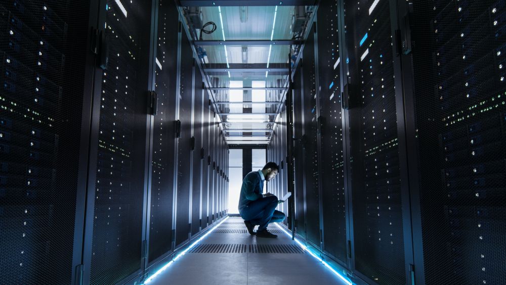 IT Technician Works on Laptop in Big Data Center full of Rack Servers.