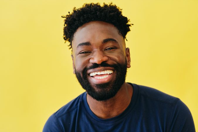 Portrait of joyful Black man in navy t-shirt in yellow studio