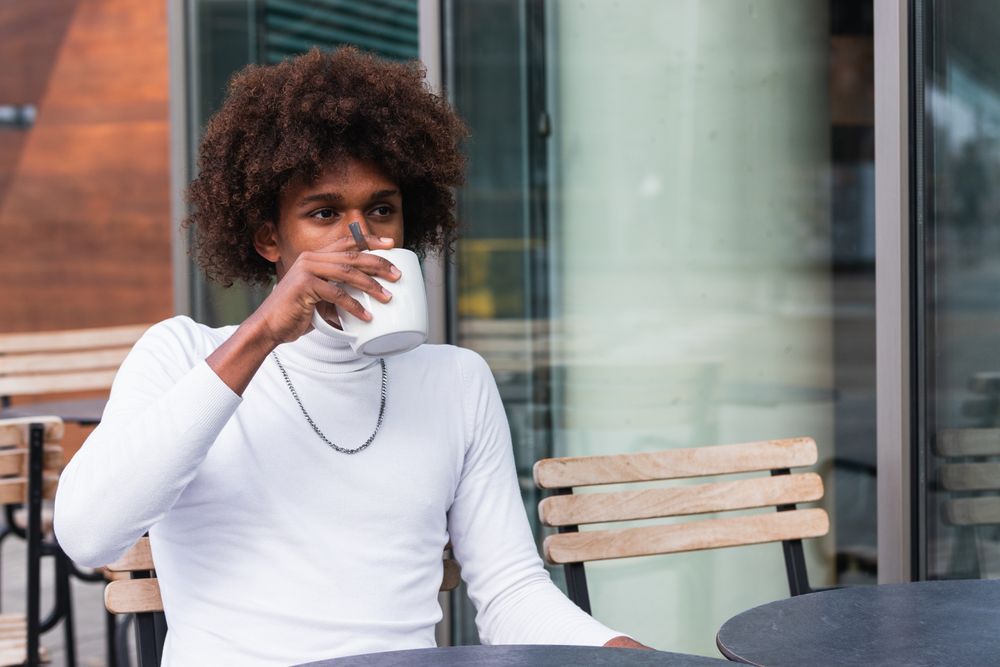 Pensive young Black man drinking coffee and looking away in cafe