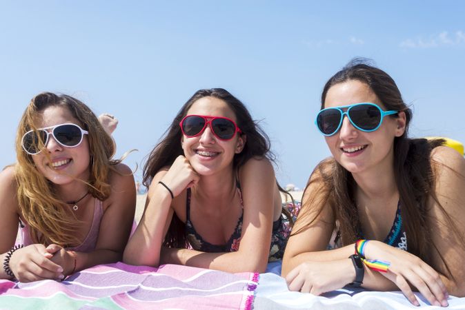 Smiling teenage girls lying on beach while looking at camera