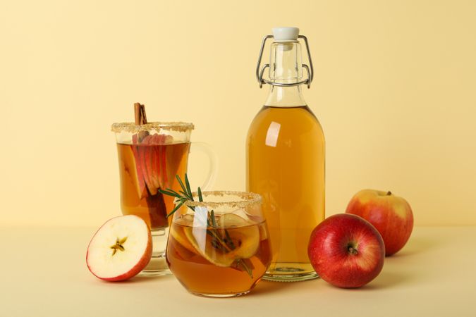 Glasses and bottle with apple cider and red apples on beige background