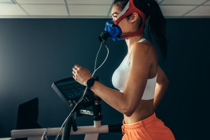Side view of professional sportswoman with mask running on treadmill in gym