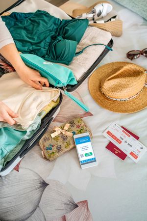 Woman preparing suitcase for vacation and mobile phone with covid green pass