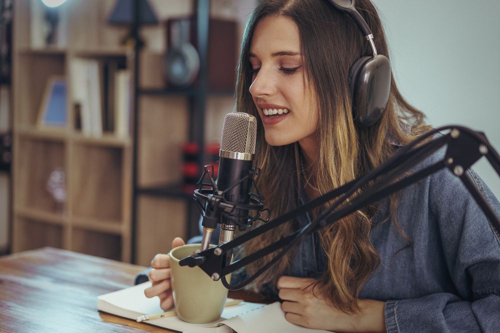 Woman recording podcast with microphone, headphones, and coffee at desk workspace