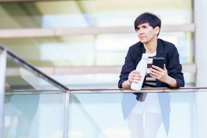 Woman taking break from work leaning outside of building with phone and bottle