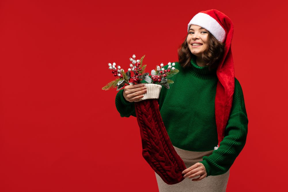 Woman in Santa hat holding Christmas stocking filled with decorations