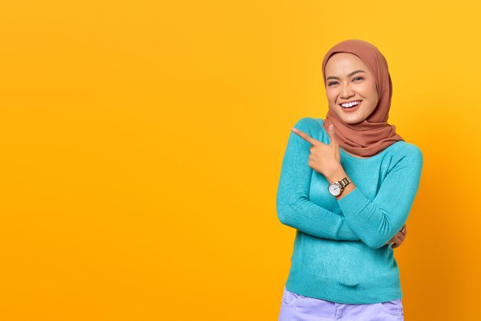 Muslim woman pointing to the side in yellow studio