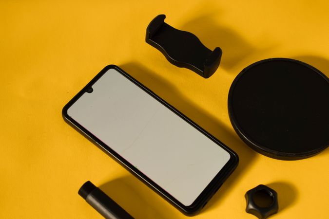 Phone with mockup screen and accessories scattered on yellow table with shadow