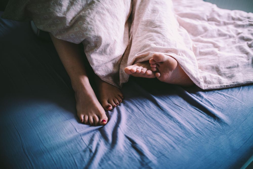 Two pairs of feet emerge from under the blankets
