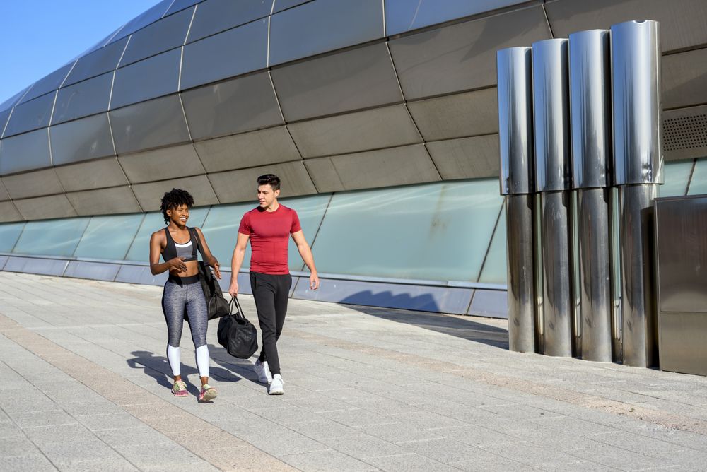 Happy sportive man and woman walking along wall in city