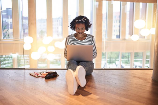 Woman sitting on floor smiling and working on her laptop on second story