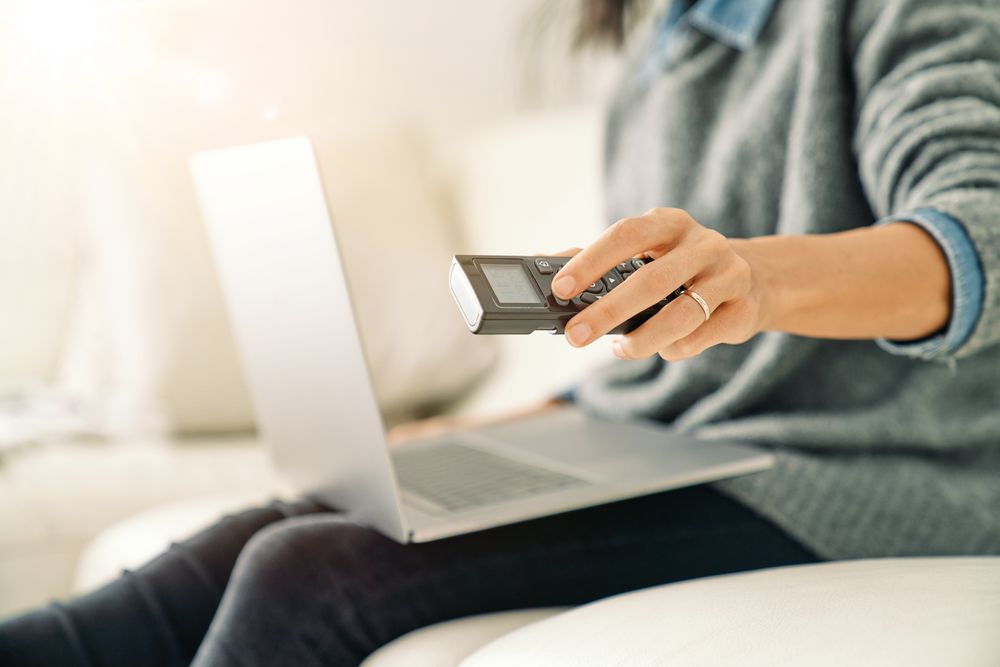 Woman pressing button on remote control while working on laptop