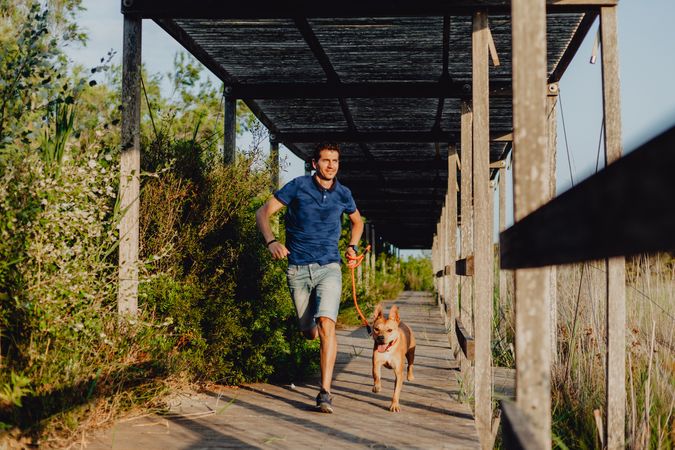 Happy adult man running with dog along countryside